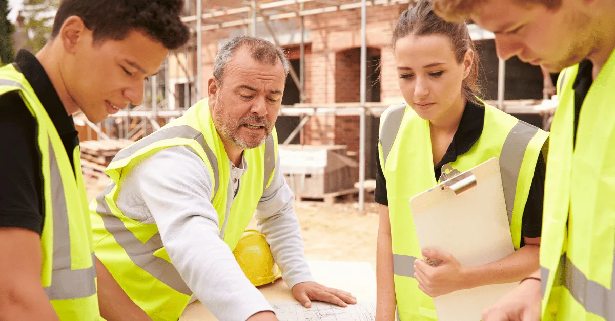 Construction team in safety vests reviewing plans at an apartment building job site.