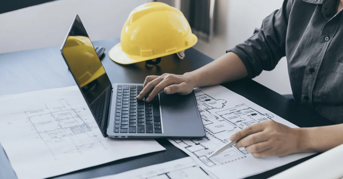 Construction professional using laptop while reviewing multifamily development blueprints.